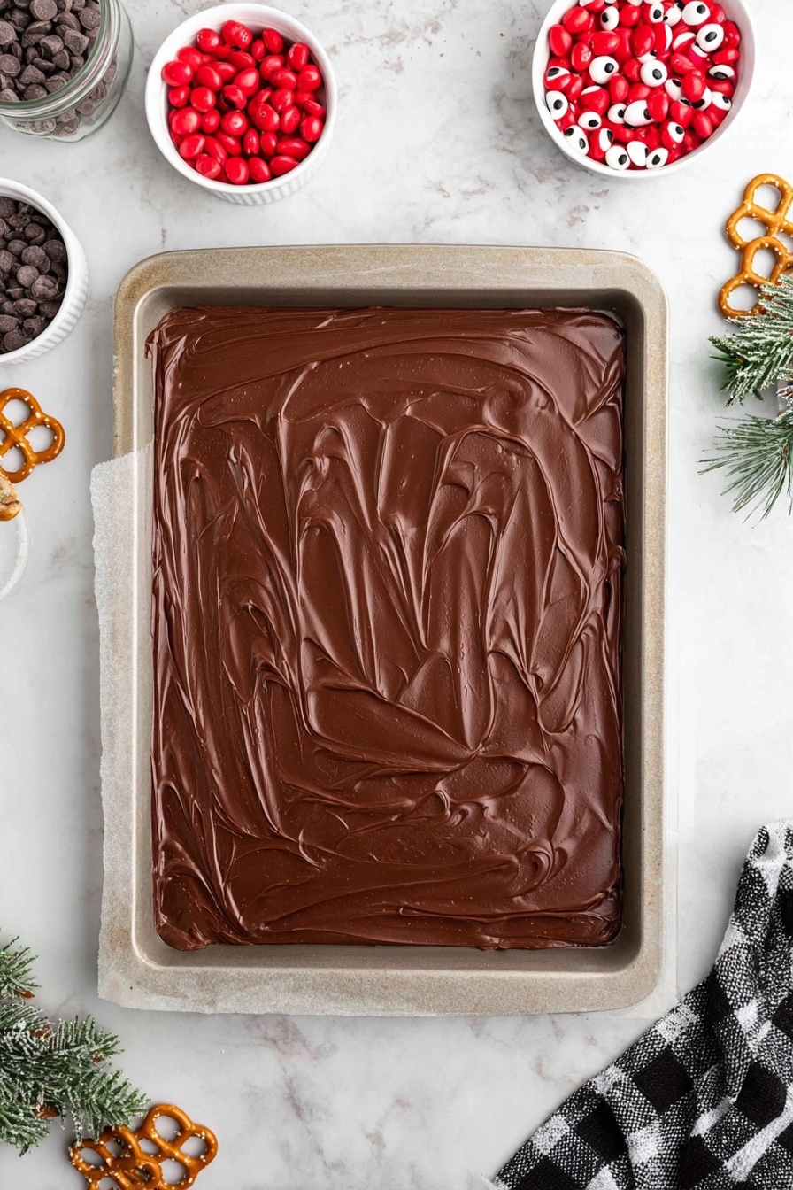 Peppermint Reindeer Chocolate Bark, festive holiday chocolate treats, holiday reindeer candy, easy Christmas chocolate bark, peppermint chocolate dessert - A stack of dark brown chocolate squares sits on crumpled white paper on a white marbled surface. Each square has two white candy eyes with black centers near the middle and a round red candy below them, resembling a nose. On top of the uppermost square, two broken small pretzel pieces shaped like antlers with a light golden color are placed near the top edge. Small white crumbs and tiny red and white candy bits are scattered over the chocolate surfaces. In the background, there is a white plate with bright red candies that look like peanuts, a white doughnut-shaped object, and a white bowl with striped red and white peppermint candies. A corner of a white and black checkered cloth is visible near the bottom right corner of the image. Photo taken with an iphone --ar 2:3 --v 7