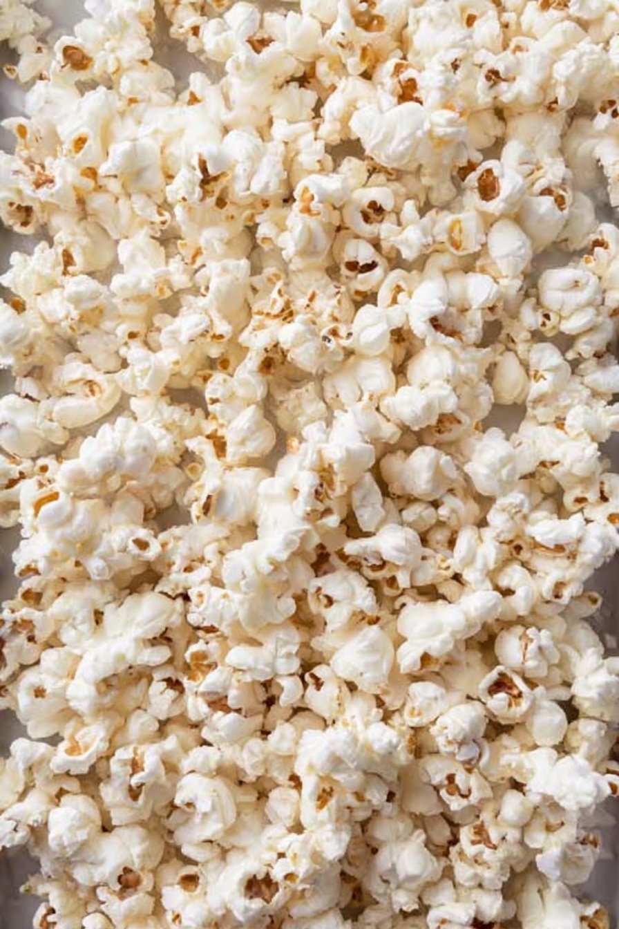 Christmas Crunch Popcorn, holiday popcorn snack, festive popcorn recipe, Christmas party snacks, easy holiday treats - The image shows a white bowl filled with a festive popcorn snack that has three main layers: the bottom layer is white popcorn, the middle layer includes broken pretzel sticks and red and green candy-coated chocolates, and the top layer is decorated with green and red sprinkles. The popcorn looks lightly coated with a white sticky layer holding everything together. The bowl is placed on a white marbled surface with scattered candies and mini marshmallows around it. In the background, there is a red, green, and white plaid cloth. photo taken with an iphone --ar 2:3 --v 7