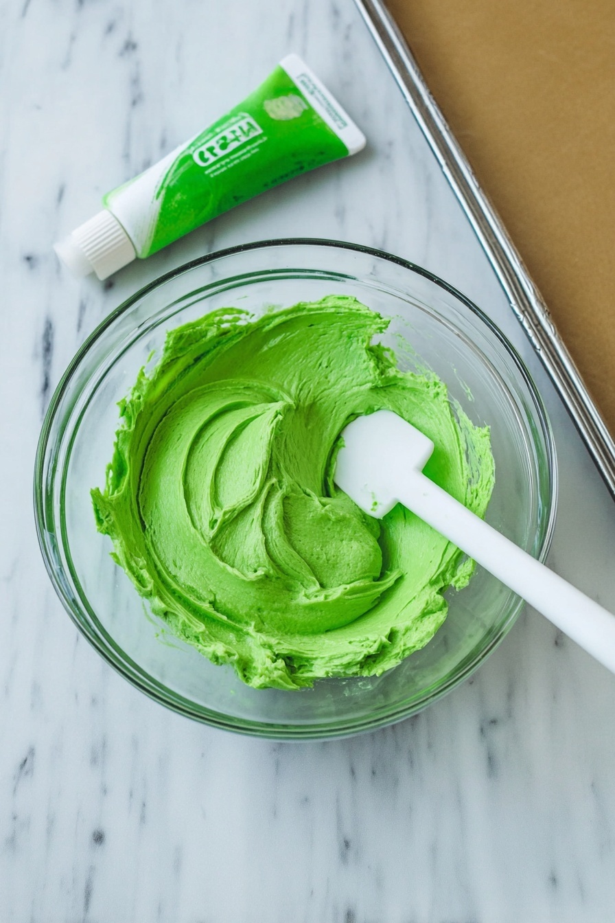 Grinch Green Cake Mix Cookies, festive holiday cookies, easy Christmas cookie recipe, green cookies for Christmas, kid-friendly holiday treats - The image shows green round cookies with cracked surfaces arranged in rows on a black cooling rack over a wooden table. Each cookie has one small red heart placed in the center on top. A red and white checkered cloth is partially visible on the left side of the frame. The cookies have a light dusting of powdered sugar on their green tops. photo taken with an iphone --ar 2:3 --v 7